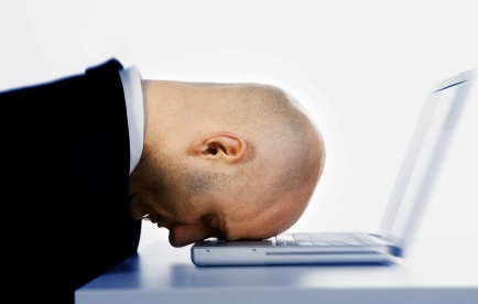 A stressed bald businessman with his forehead resting on the laptop computer keyboard.